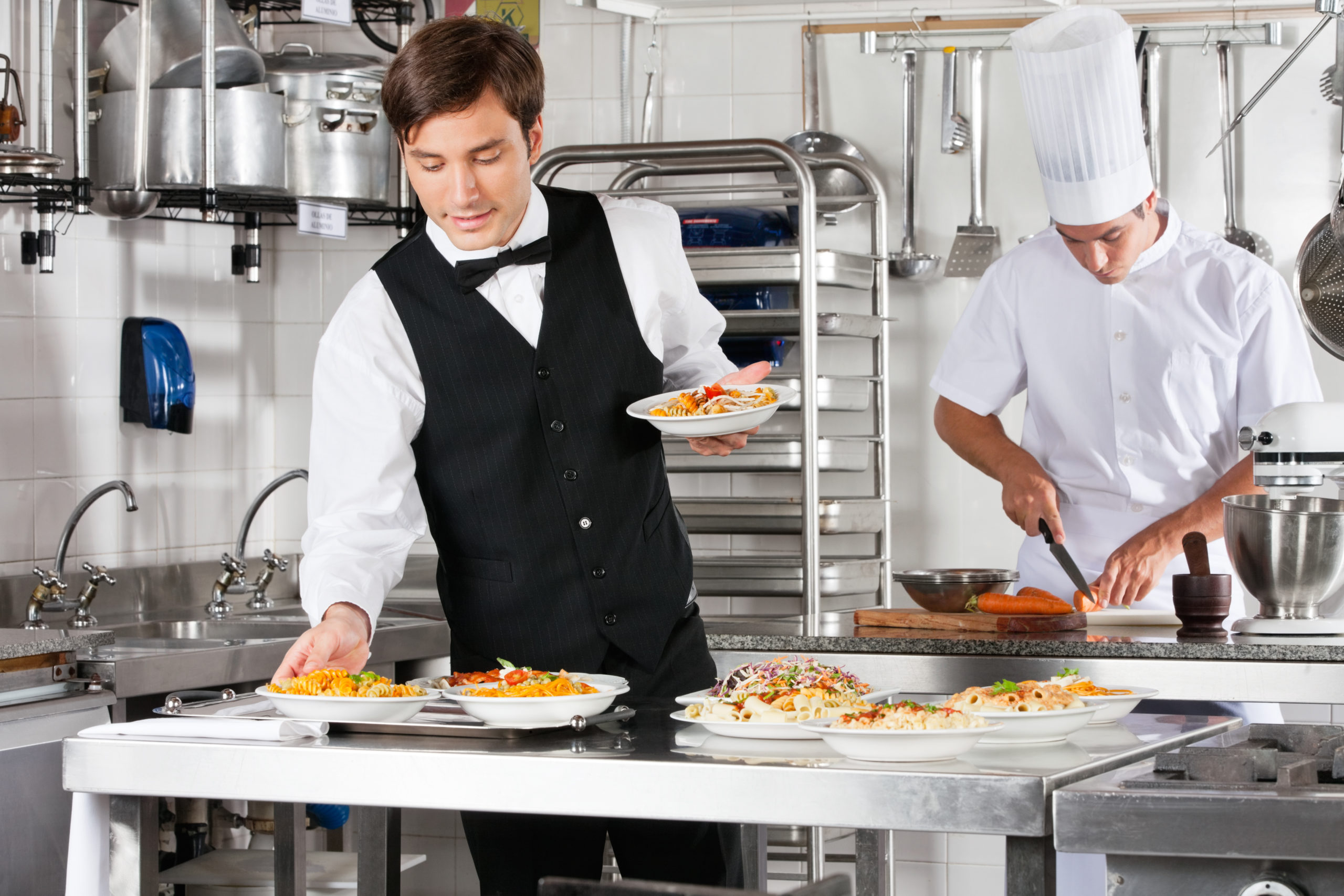 Waiter And Chef Working In Commercial Kitchen